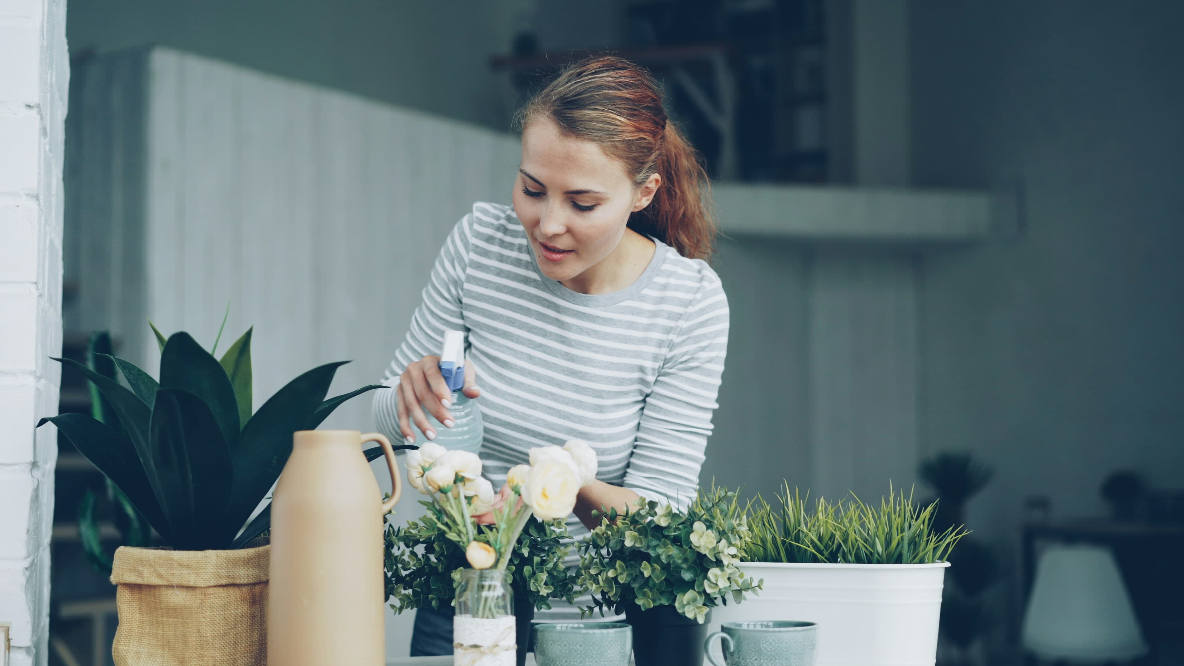 person watering potted plants on apartment balcony in morning sunlight
